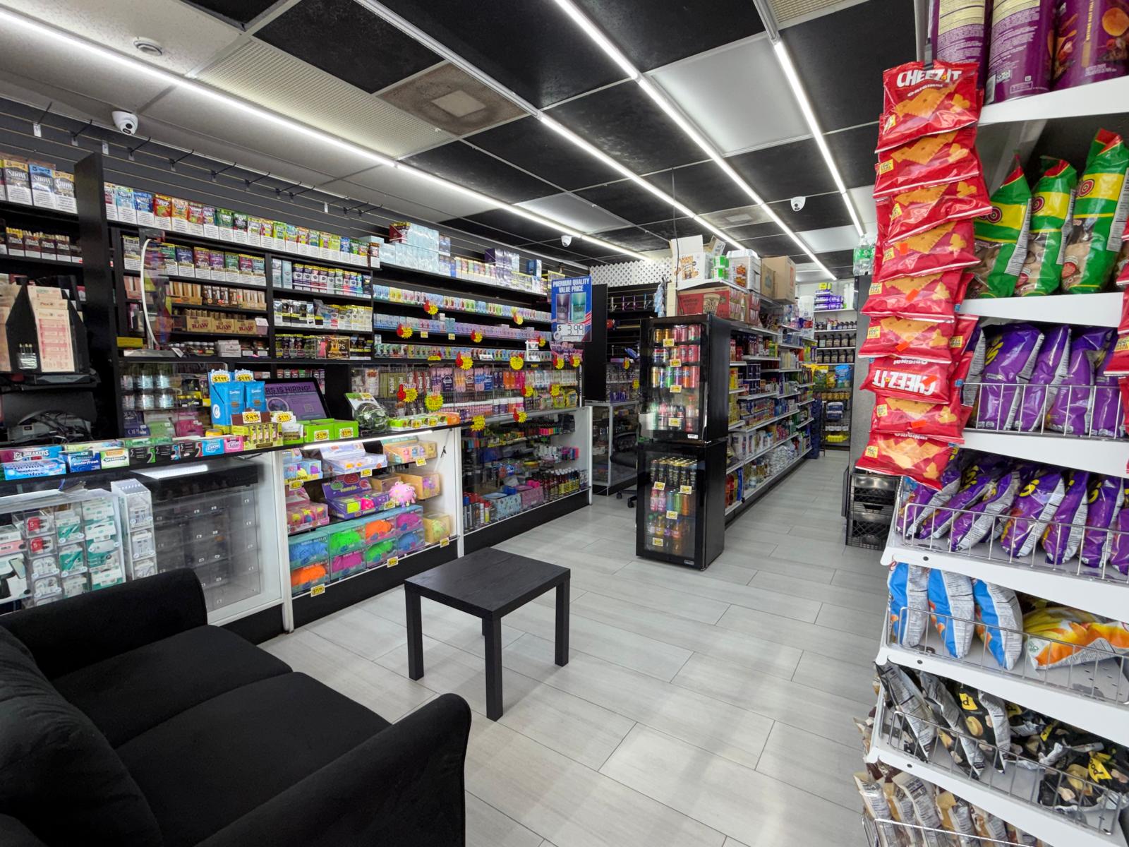 Interior of One Stop Market N Smoke Shop in Hialeah, FL with customer seating area, vape display wall, drink cooler, and snack aisle.