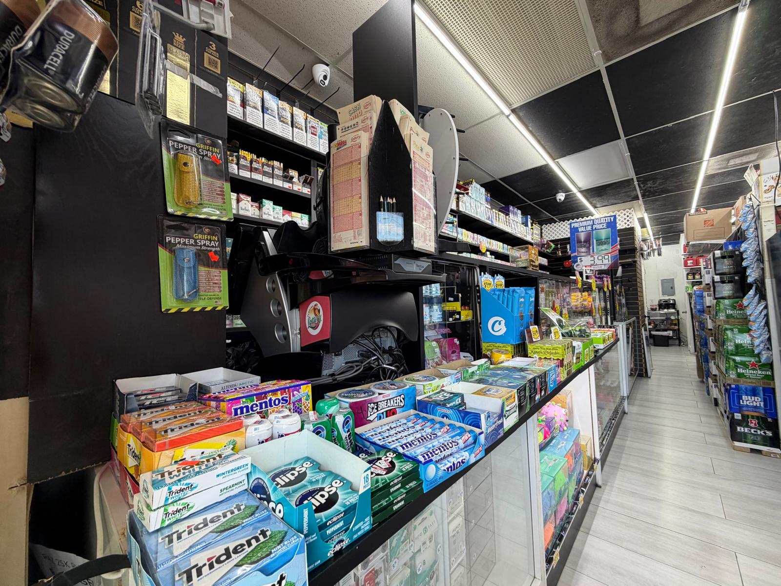 Front checkout counter at One Stop Market N Smoke Shop in Hialeah, FL with gum, mints, lottery tickets, and beer coolers in the aisle.