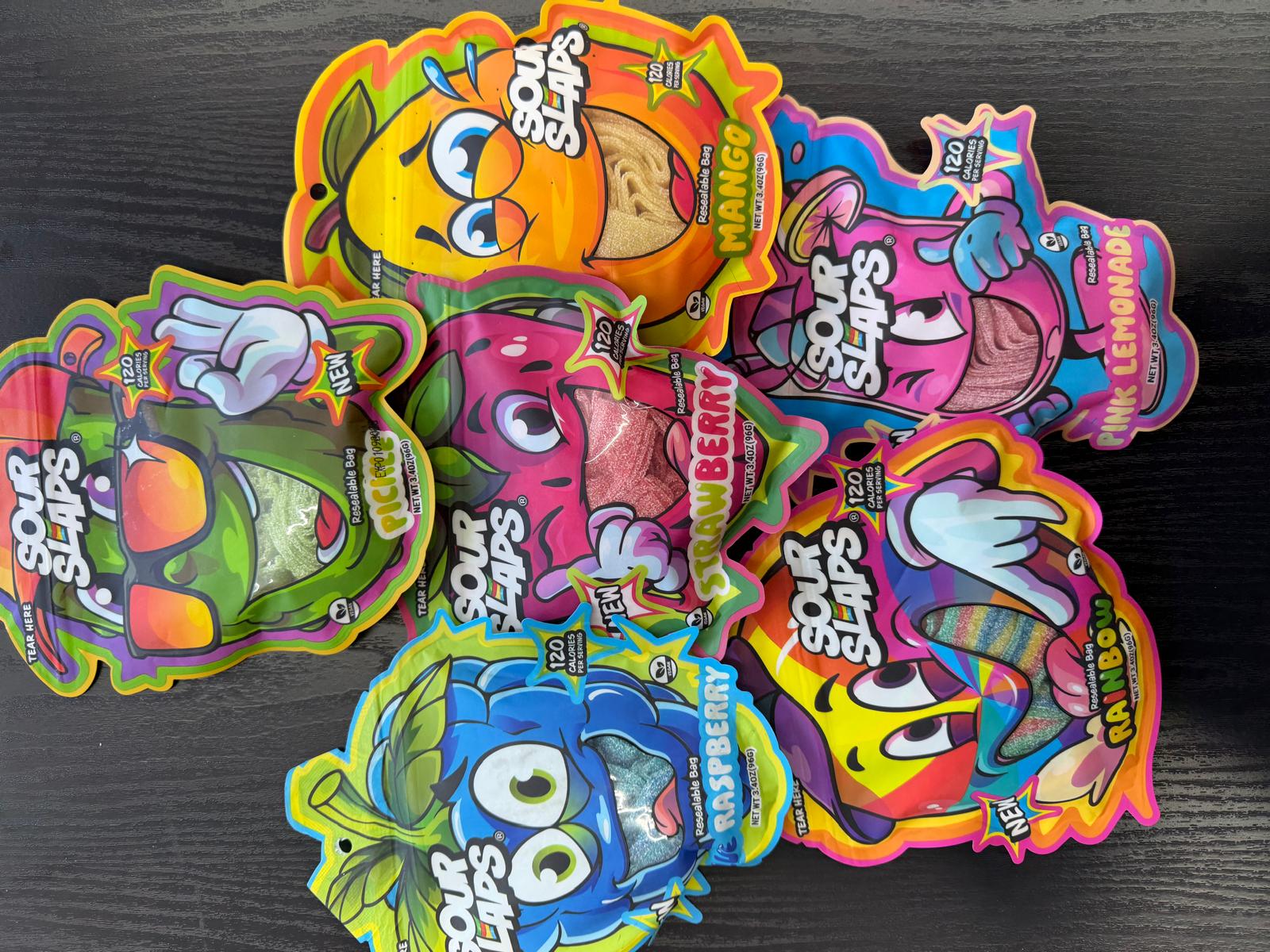 Assorted Sour Slaps sour candy bags in mango, strawberry, raspberry, pink lemonade, pickle, and rainbow flavors.