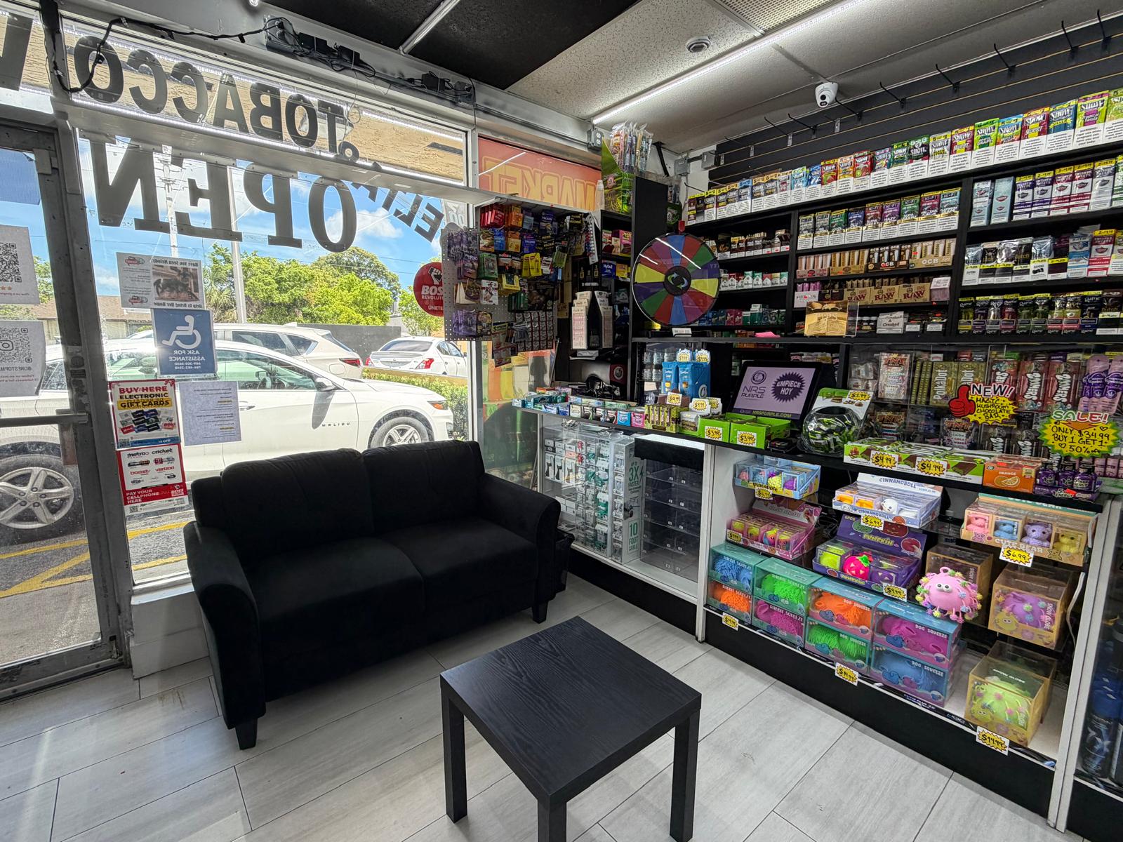 Entrance and customer seating area at One Stop Market N Smoke Shop in Hialeah, FL with Tobacco Open sign in the window.