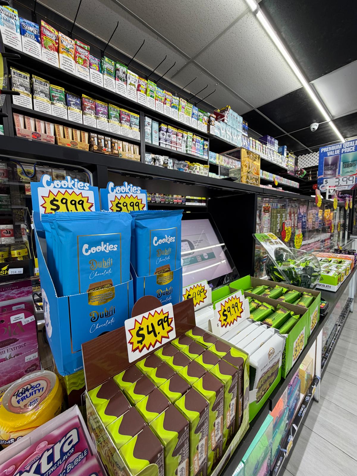 Candy and Dubai chocolate display at One Stop Market N Smoke Shop in Hialeah, FL with rolling papers and cigarillos on shelves behind.